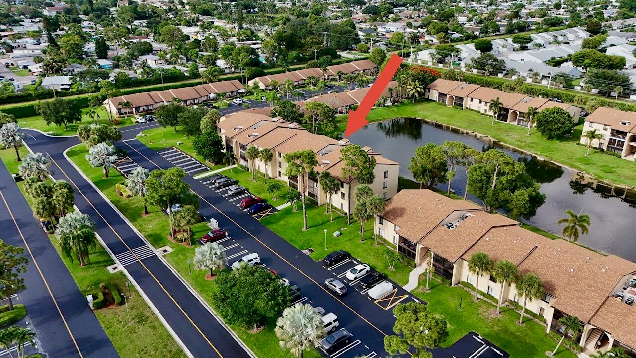 An aerial view shows a multi-story apartment building with a parking lot and a pond — 627 Sea Pine Way # C2, FL 33415, FL