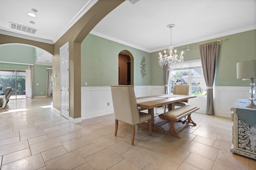 A dining room with sage green walls, white wainscoting, a crystal chandelier, and tile flooring — 5210 SPARROWGLEN PLACE, LITHIA, FL