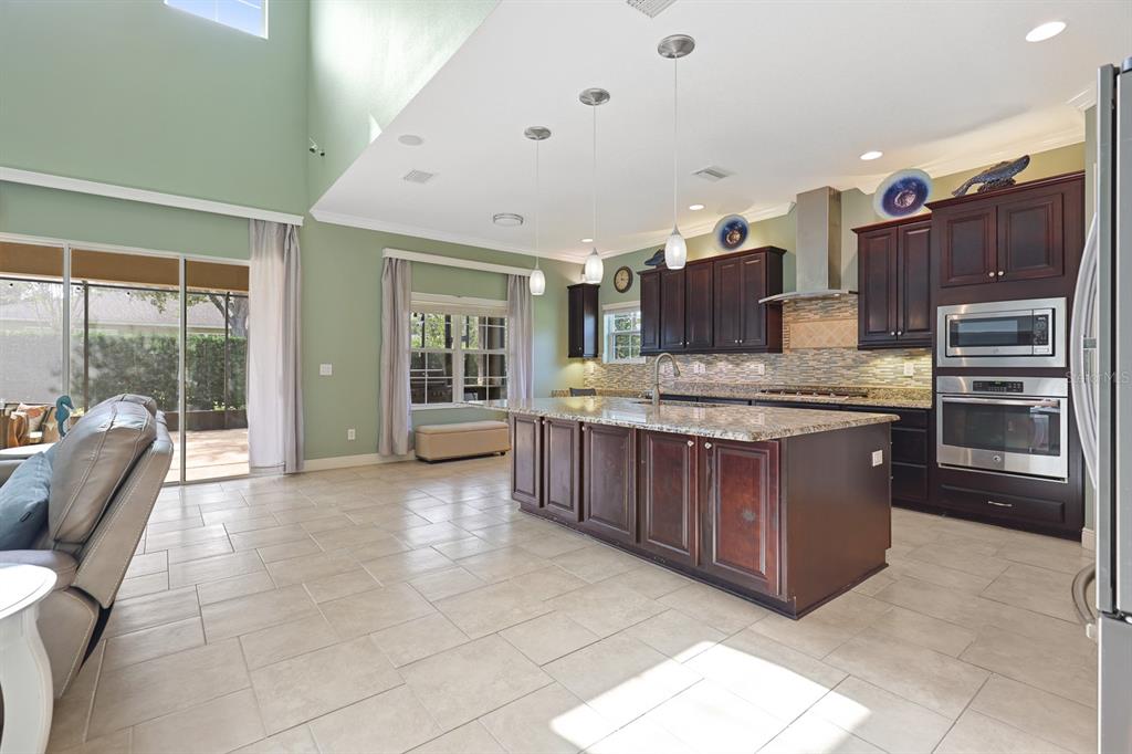 A kitchen with dark wood cabinets, granite countertops, and an island opens to a living area — 5210 SPARROWGLEN PLACE, LITHIA, FL