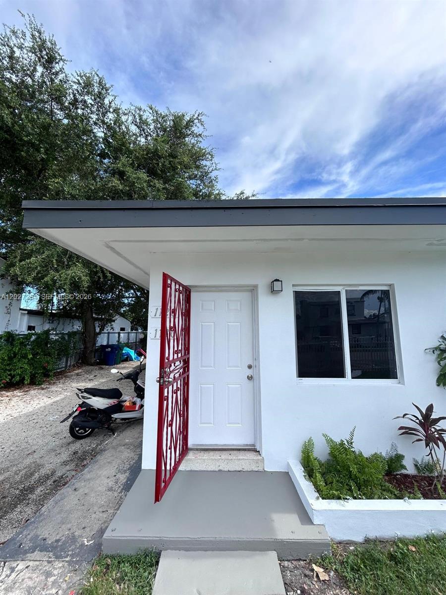 A white exterior wall features a white door with a red metal security gate — 1130 NW 76th St # 1130, Miami FL 33150, MIAMI, FL