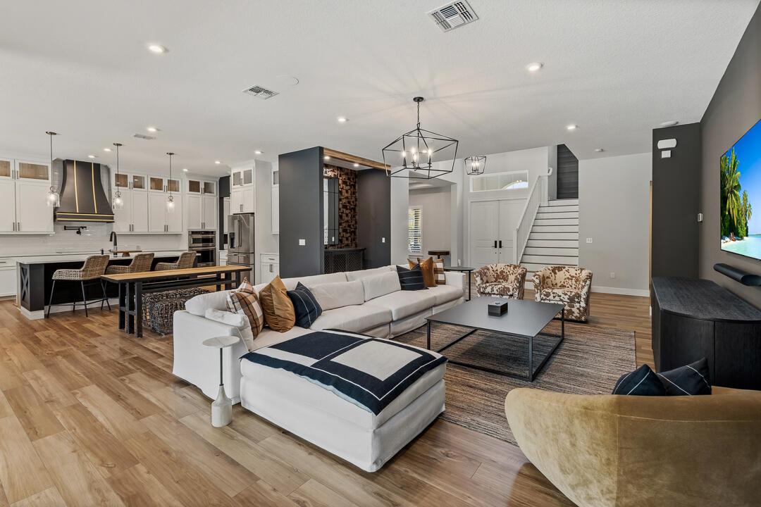 An open-concept living room and kitchen featuring white cabinetry, wood flooring, and modern lighting — 2465 NE Evinrude Circle, Jensen Beach FL 34957, JENSEN BEACH, FL