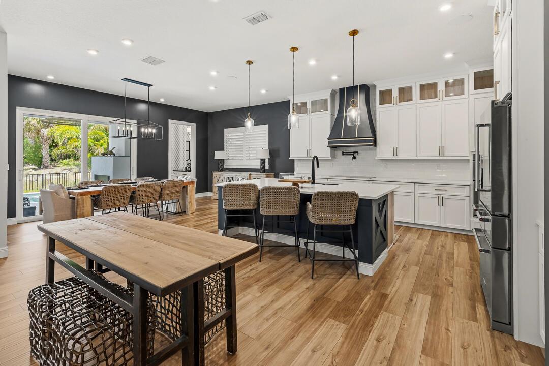 A kitchen and dining area with white cabinets, a dark island, and wood-look flooring — 2465 NE Evinrude Circle, Jensen Beach FL 34957, JENSEN BEACH, FL
