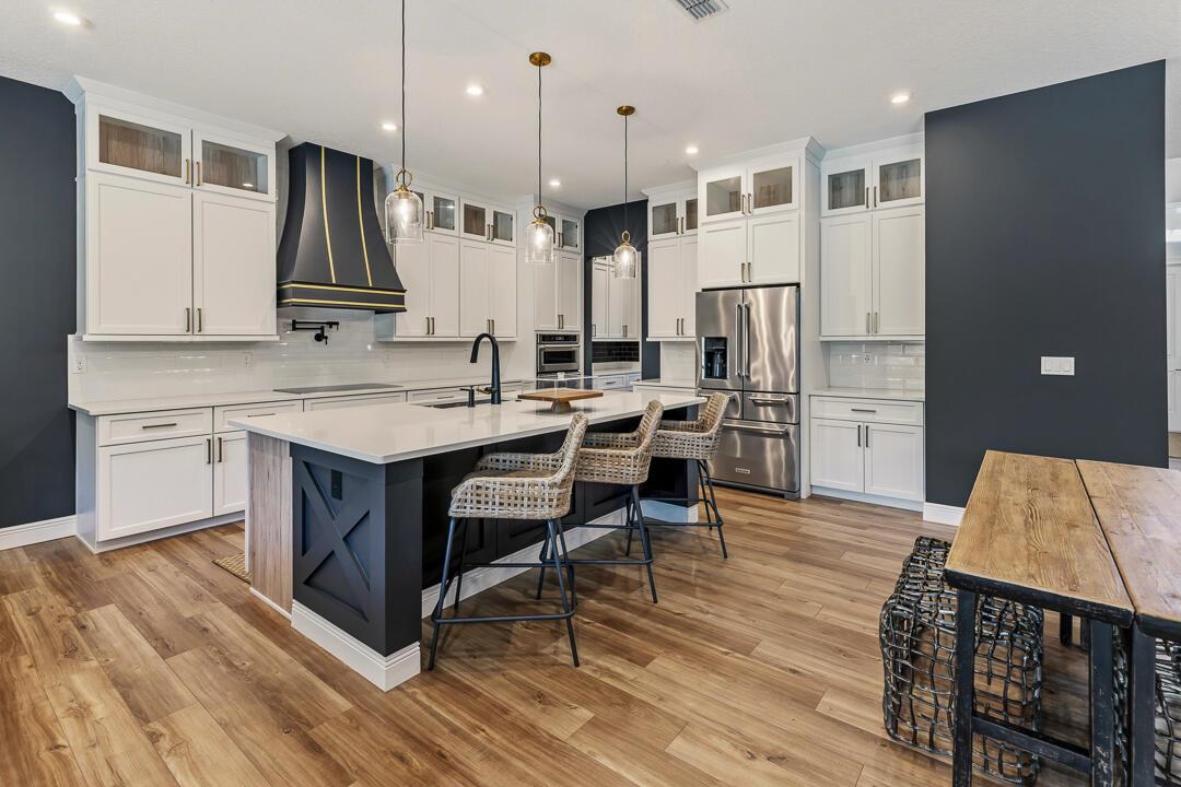 A modern kitchen features white cabinetry, a dark island with seating, and wood-look flooring — 2465 NE Evinrude Circle, Jensen Beach FL 34957, JENSEN BEACH, FL