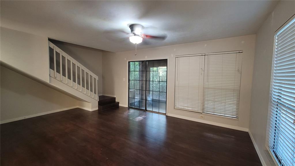 A living room with dark wood floors, a ceiling fan, a staircase, and sliding glass doors — 819 SW 57TH TERRACE, GAINESVILLE, FL