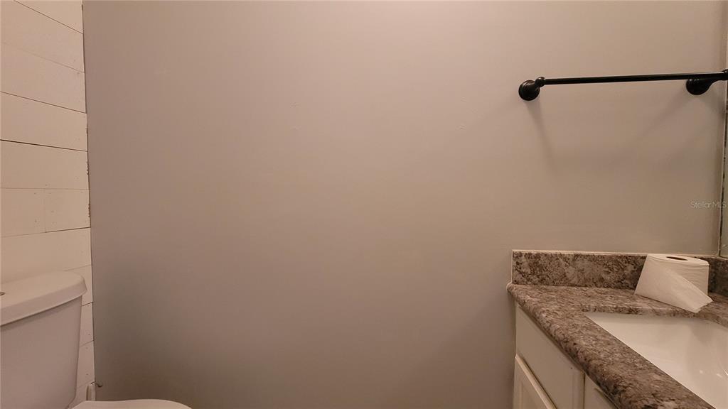 A bathroom features a white toilet, a vanity with a stone countertop, and shiplap walls — 819 SW 57TH TERRACE, GAINESVILLE, FL