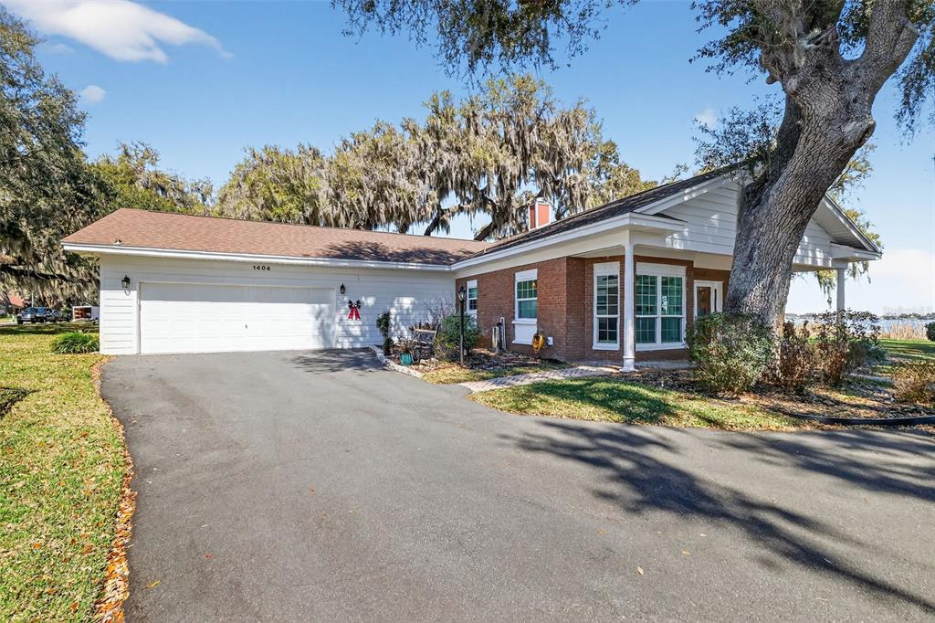 A brick and white siding house features a two-car garage and a large oak tree — 1404 REGENCY COURT, LEESBURG, FL