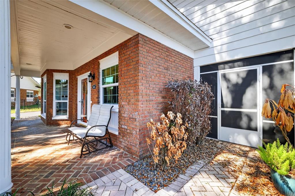A brick-paved front porch features a white rocking chair and a screened-in entryway — 1404 REGENCY COURT, LEESBURG, FL