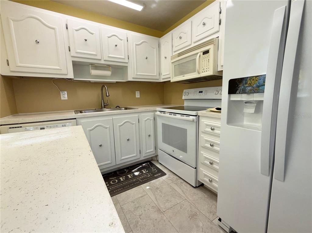 A kitchen features white cabinetry, white appliances, light countertops, and a tiled floor — 11817 BAYONET LANE, NEW PORT RICHEY, FL