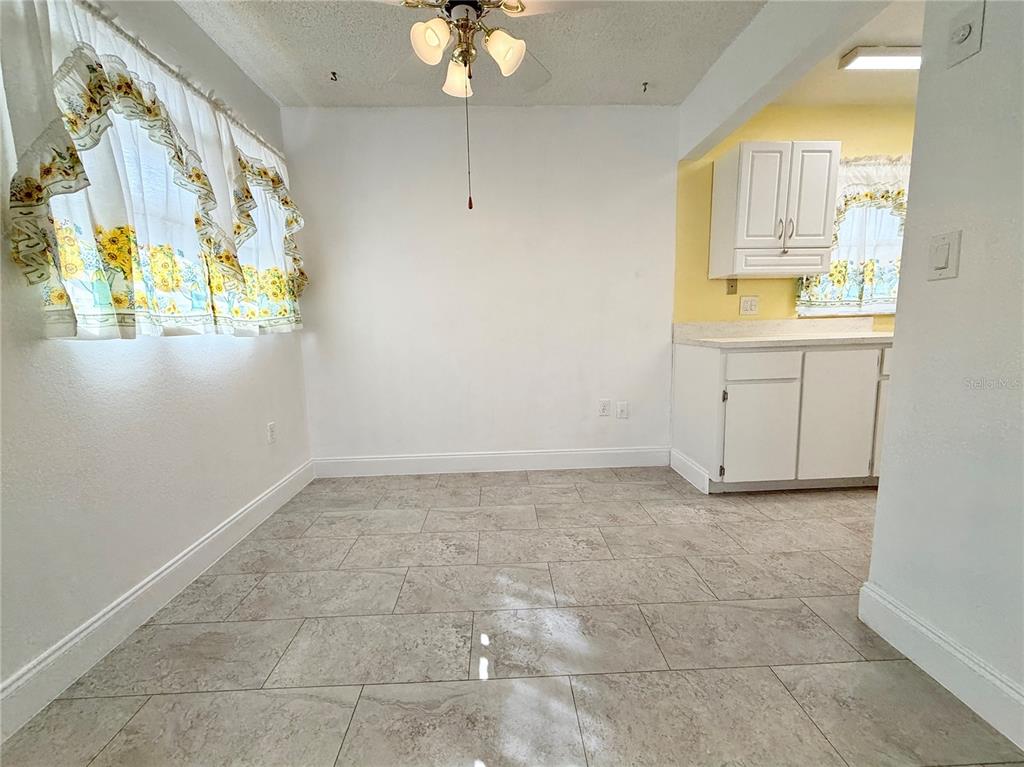 A dining area features light-colored tile flooring, white walls, and a sunflower-patterned window valance — 11817 BAYONET LANE, NEW PORT RICHEY, FL