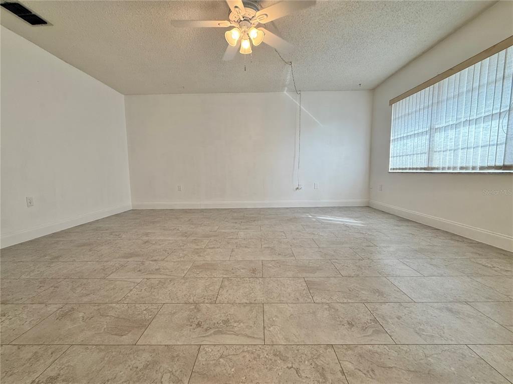 An empty room features white walls, a ceiling fan, and light-colored rectangular floor tiles — 11817 BAYONET LANE, NEW PORT RICHEY, FL