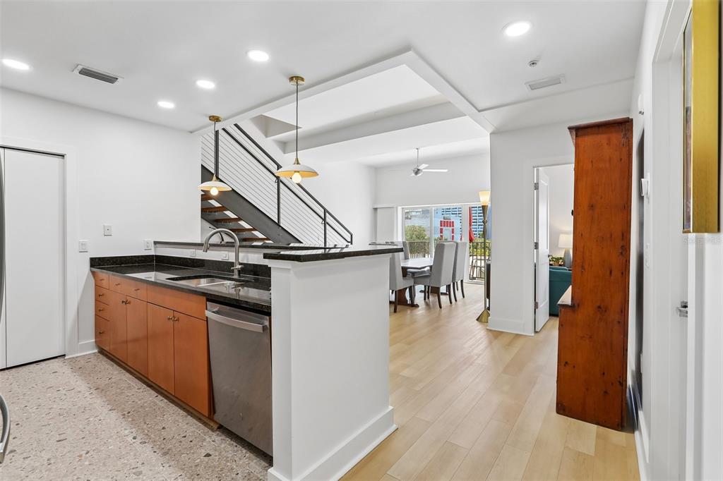 A kitchen with wood cabinets and granite countertops overlooks a dining area and staircase — 1010 CENTRAL AVENUE UNIT 413, ST PETERSBURG, FL