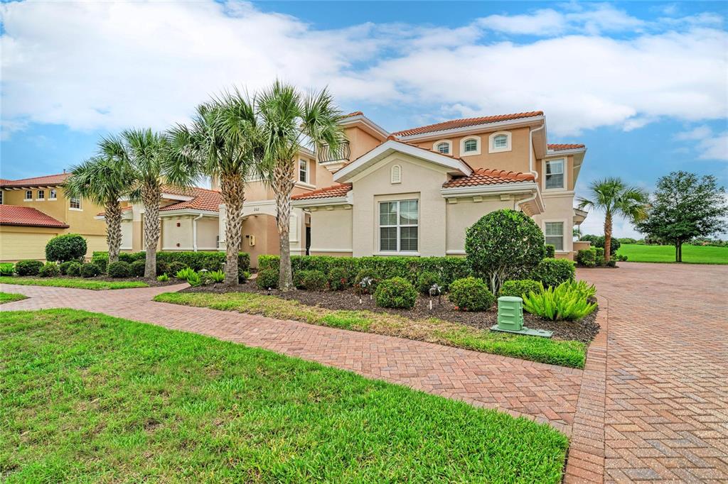 A two-story stucco house with a tile roof, palm trees, and a brick paver driveway — 202 BELLA VISTA TERRACE UNIT 28D, NOKOMIS, FL