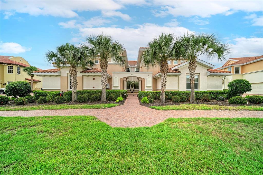 A tan two-story building with a brick walkway and palm trees in the front yard — 202 BELLA VISTA TERRACE UNIT 28D, NOKOMIS, FL