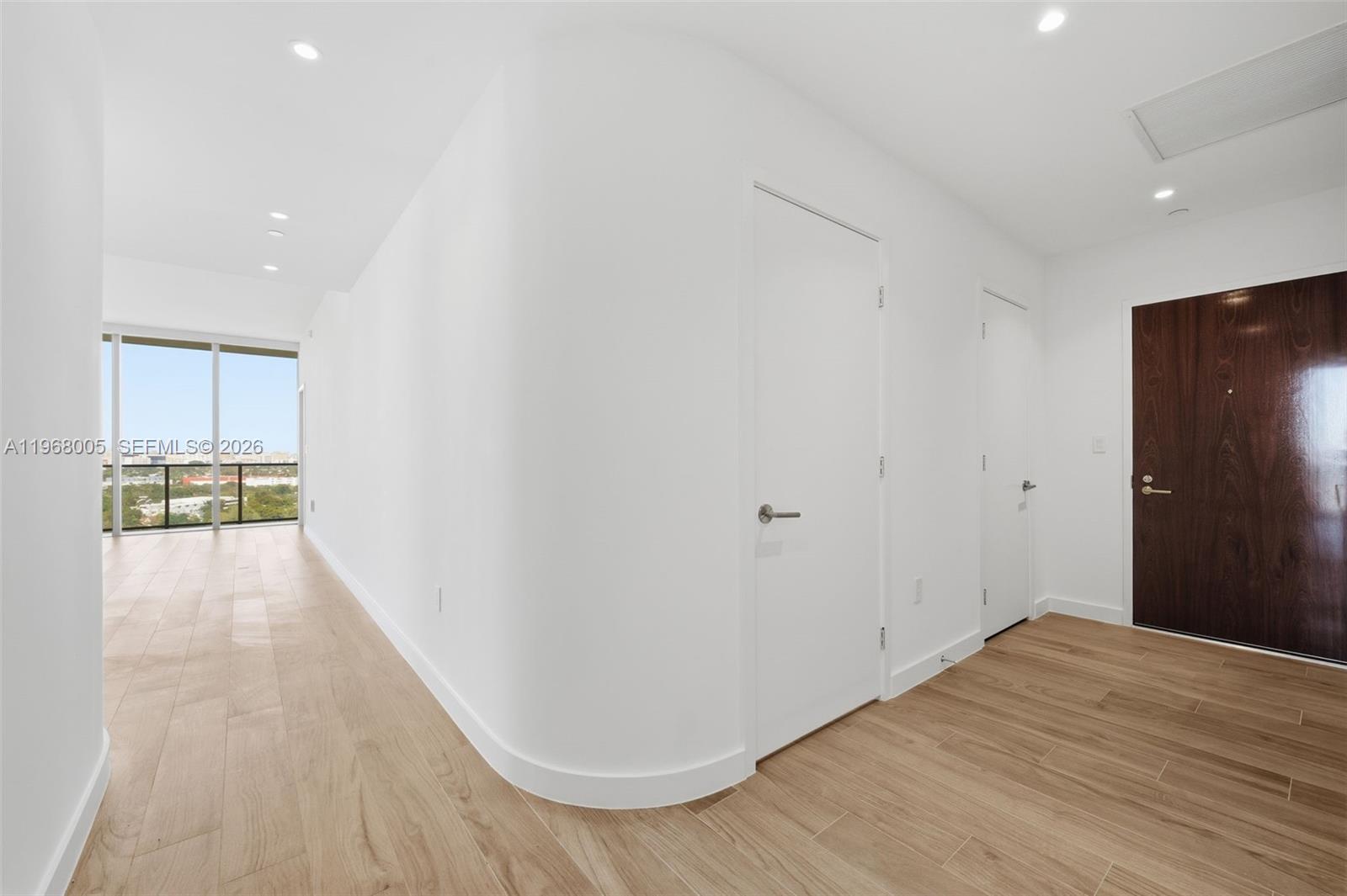 A hallway with light wood floors leads to a room with floor-to-ceiling windows — 2678 Tigertail Ave # 1501, Miami FL 33133, MIAMI, FL