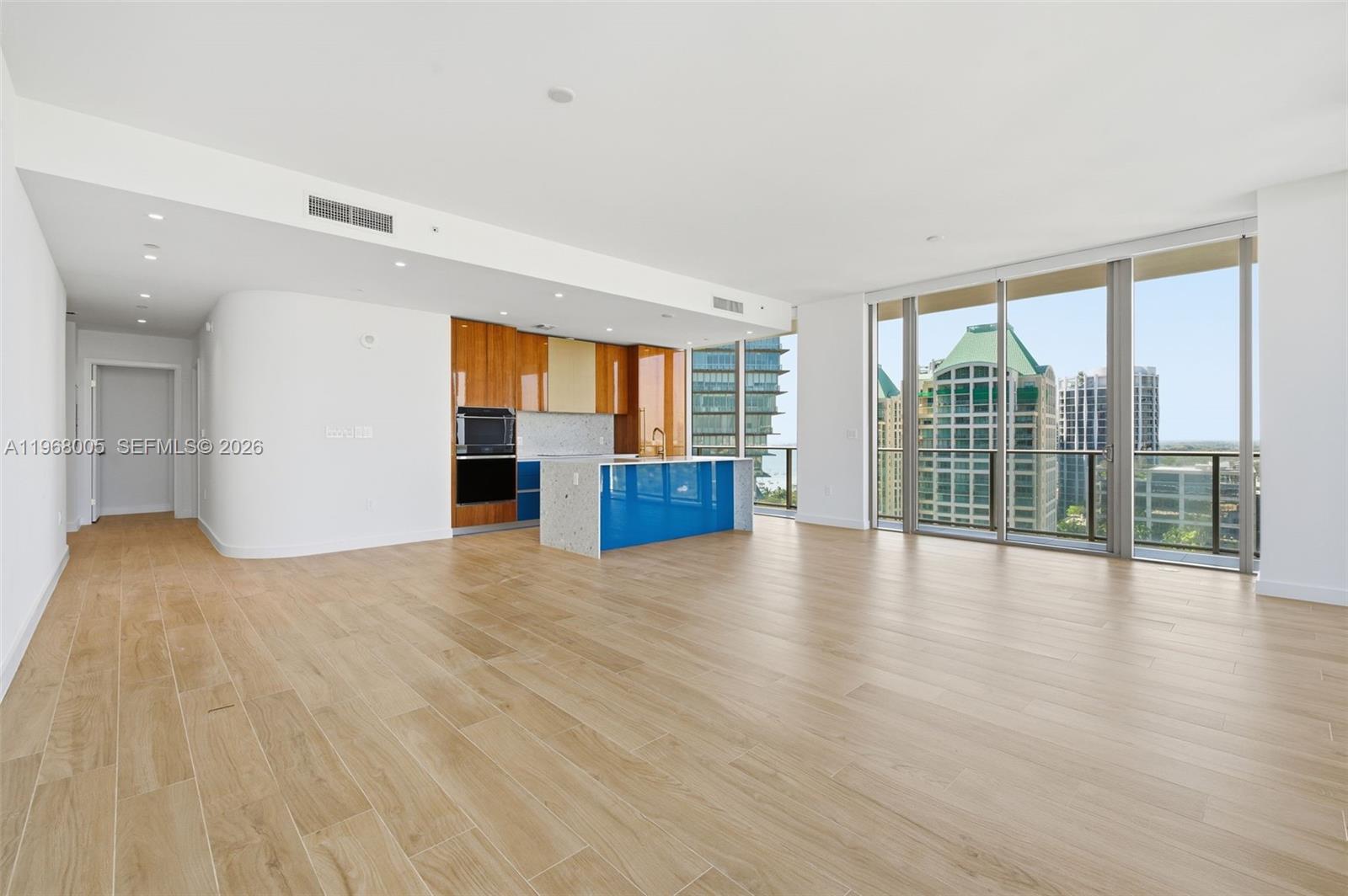 A modern open-concept kitchen with blue cabinetry and wood accents overlooks a city skyline — 2678 Tigertail Ave # 1501, Miami FL 33133, MIAMI, FL
