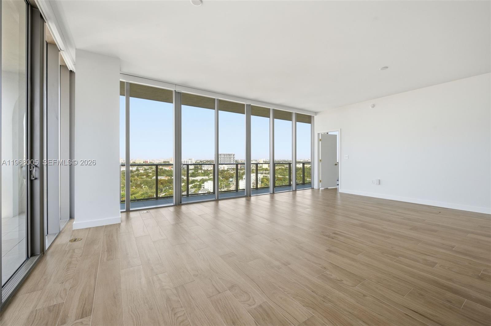 An empty room features light wood-look flooring, white walls, and floor-to-ceiling windows with balcony access — 2678 Tigertail Ave # 1501, Miami FL 33133, MIAMI, FL