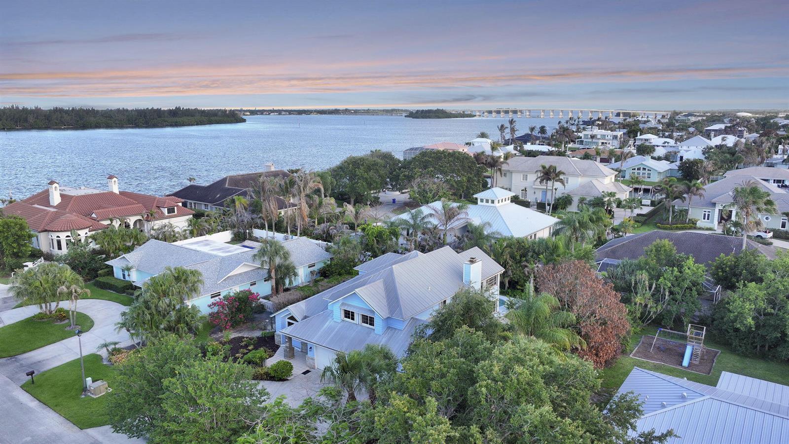 An aerial view shows a coastal neighborhood with houses, lush trees, and a large bay — 23 Sea Gull Place, Vero Beach FL 32960, VERO BEACH, FL