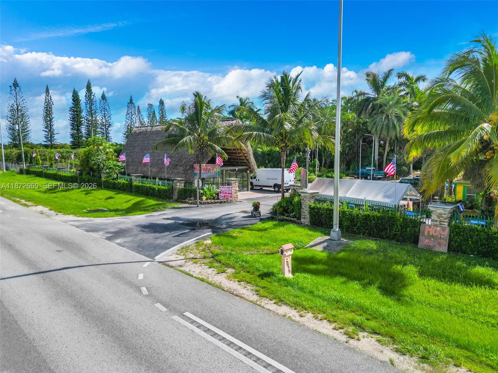 An exterior view of a plant nursery featuring a thatched-roof structure and American flags — 20425 SW 177th av, Miami FL 33187, MIAMI, FL