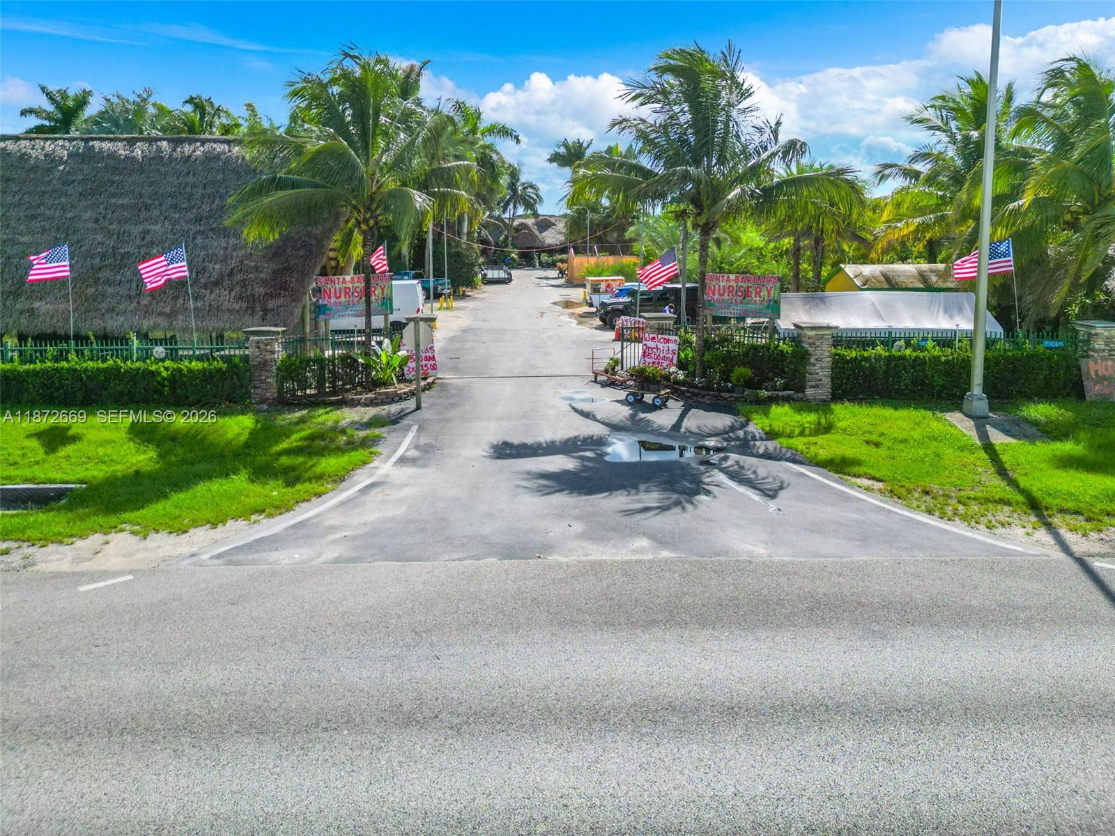 An outdoor view of a nursery entrance featuring palm trees, American flags, and signage — 20425 SW 177th av, Miami FL 33187, MIAMI, FL