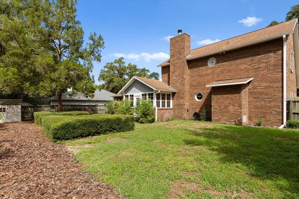 A two-story brick house with a chimney and a sunroom sits in a grassy backyard — 11617 NW 13TH LANE, GAINESVILLE, FL