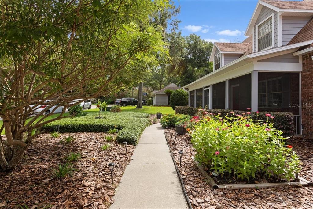 A concrete walkway leads to the screened-in porch of a house with a landscaped yard — 11617 NW 13TH LANE, GAINESVILLE, FL