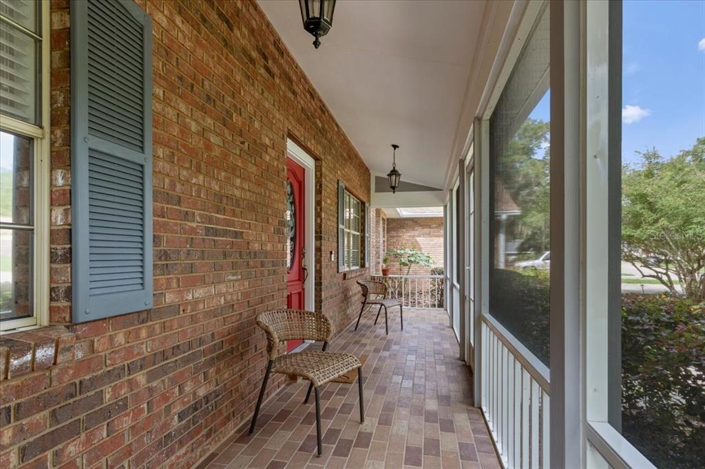 A screened-in brick porch features a red front door, tiled flooring, and two wicker chairs — 11617 NW 13TH LANE, GAINESVILLE, FL