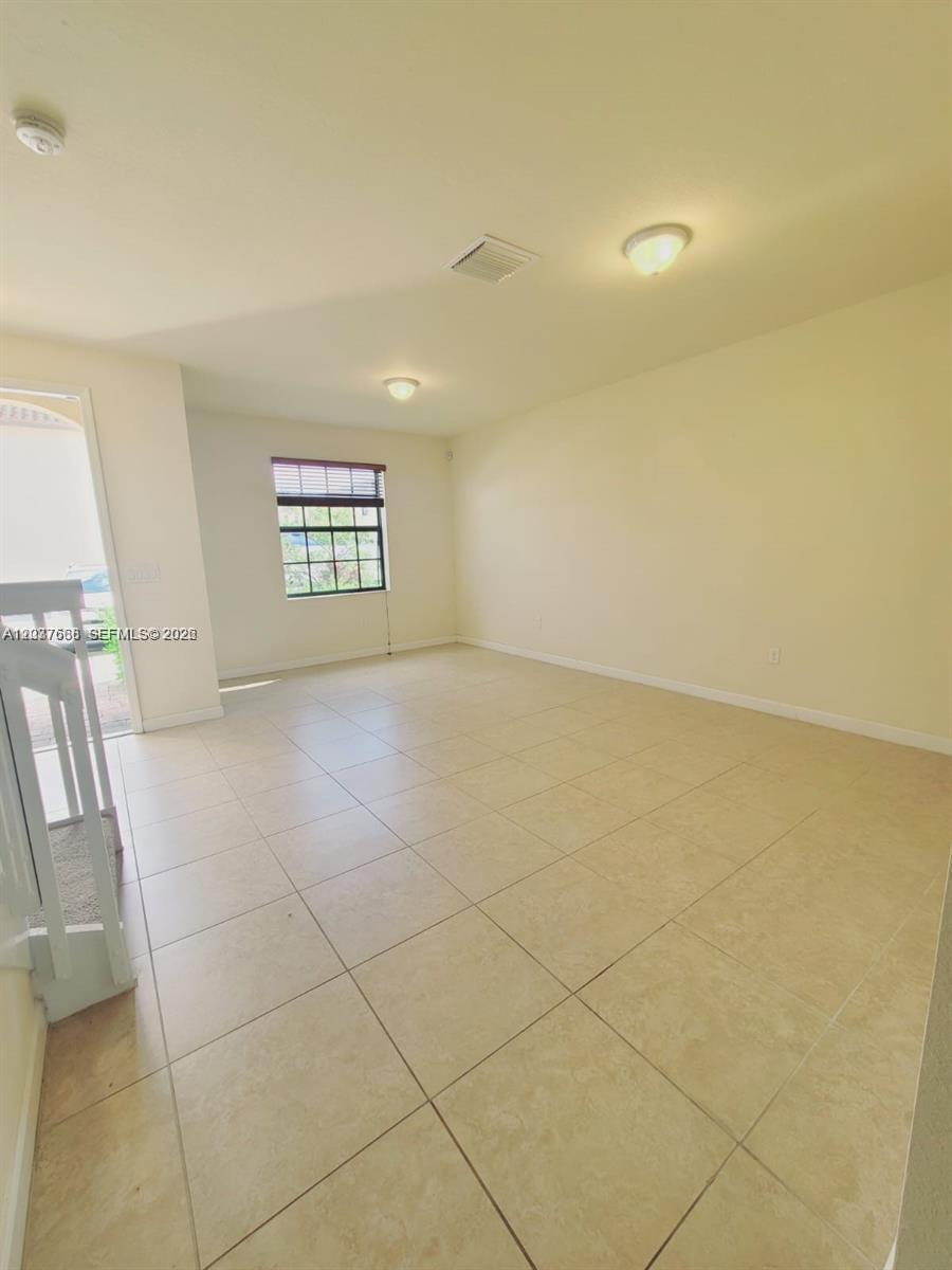 An empty room features light-colored tile flooring, beige walls, and a single window — 3537 W 89th Pl, Hialeah FL 33018, HIALEAH, FL