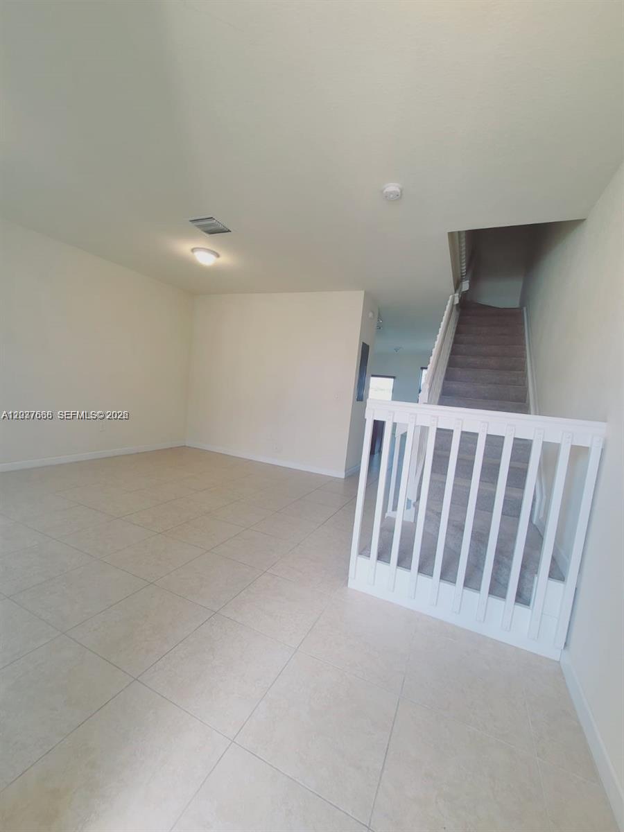 A room with light-colored tile flooring features a staircase with a white safety gate — 3537 W 89th Pl, Hialeah FL 33018, HIALEAH, FL