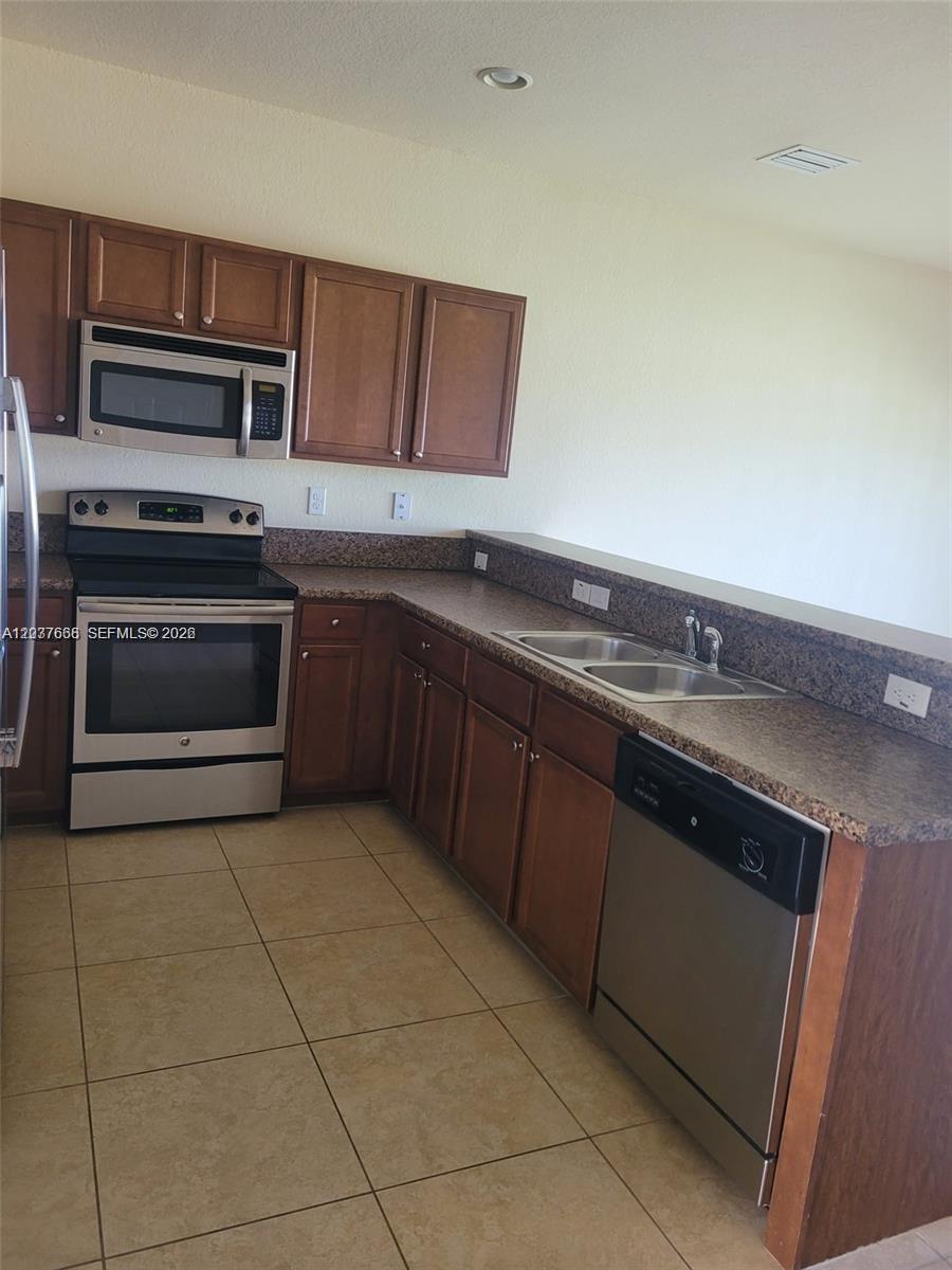 A kitchen features wood cabinets, stainless steel appliances, and granite countertops over tile flooring — 3537 W 89th Pl, Hialeah FL 33018, HIALEAH, FL