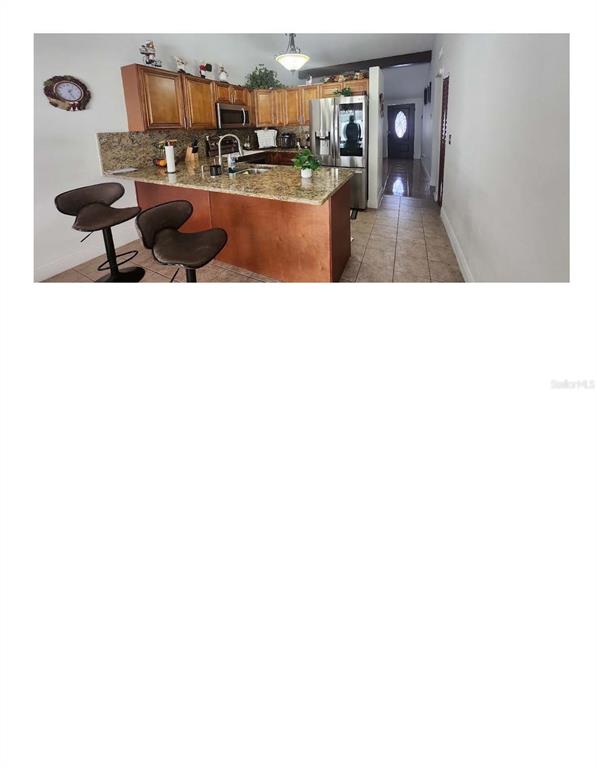 A kitchen features wood cabinets, granite countertops, a breakfast bar with stools, and tile flooring — 16009 BALLICA DRIVE, TAMPA, FL
