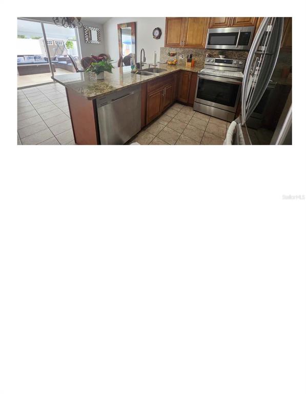 A kitchen features wood cabinets, granite countertops, stainless steel appliances, and a tile floor — 16009 BALLICA DRIVE, TAMPA, FL