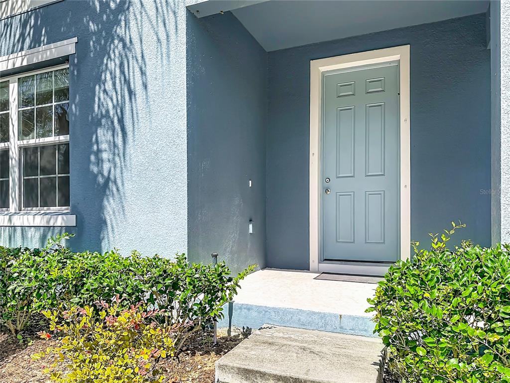 A blue front door is set within a recessed entryway next to a window and bushes — 5754 SURPRISE LILY DRIVE, WINTER GARDEN, FL