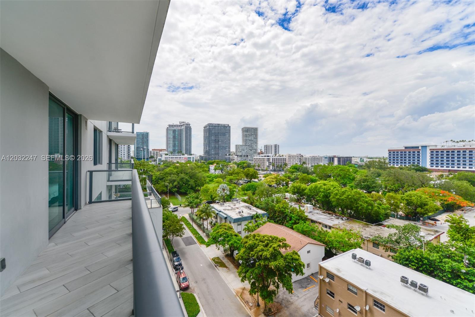 A balcony with gray tiled flooring overlooks a street, lush trees, and city high-rises — 501 NE 31st St # 601, Miami FL 33137, MIAMI, FL