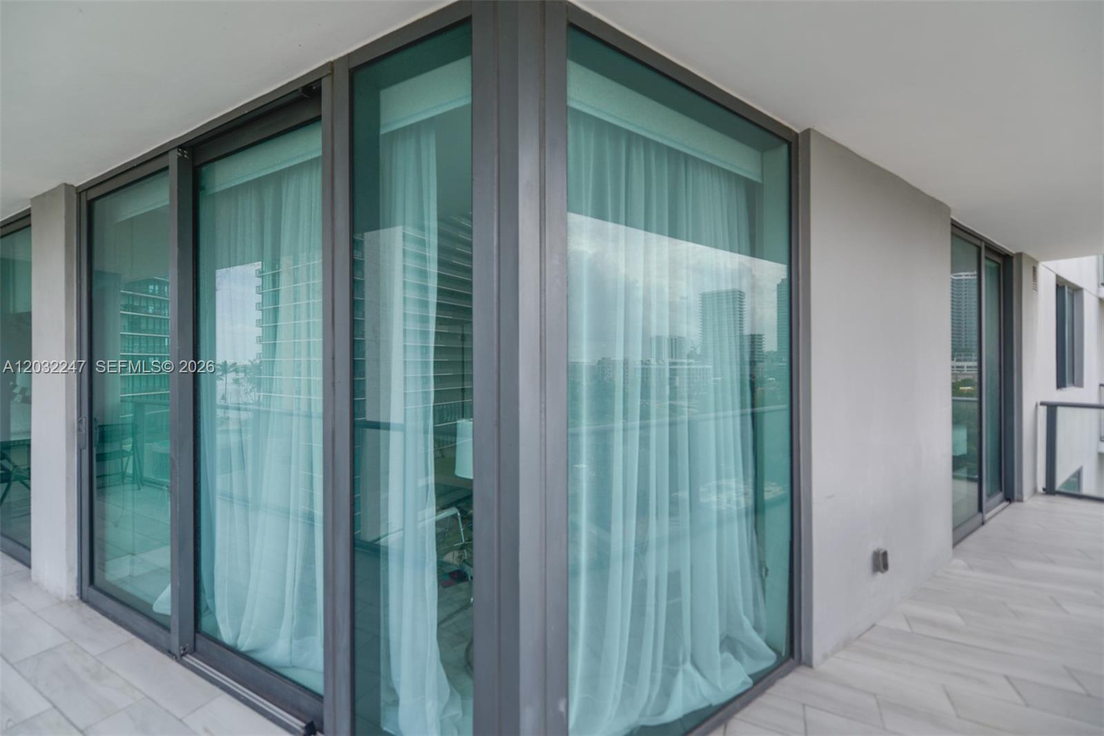 A corner balcony features floor-to-ceiling glass windows with sheer curtains and light-colored tile flooring — 501 NE 31st St # 601, Miami FL 33137, MIAMI, FL