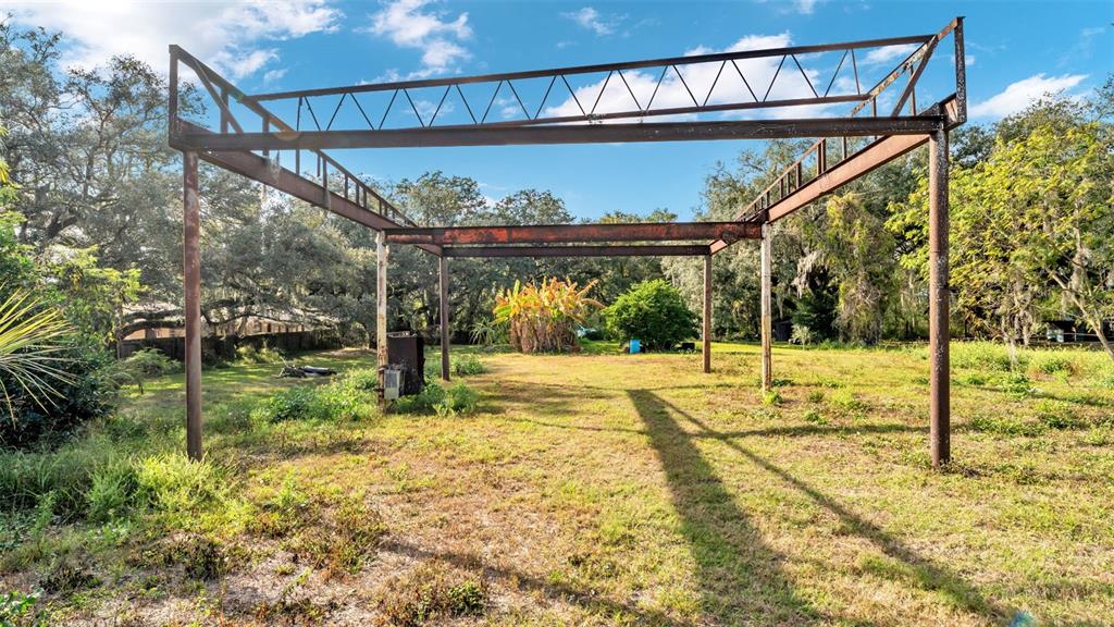 A metal structural frame stands in an open, grassy lot surrounded by trees — 23 VIOLET STREET, PLANT CITY, FL