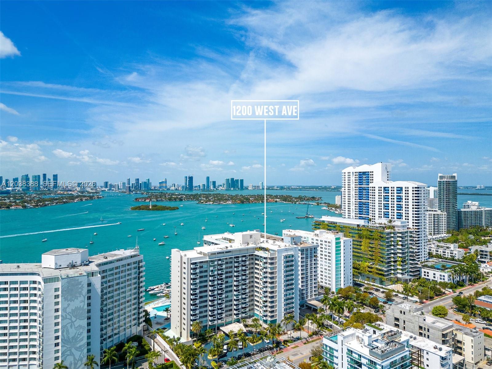An aerial view shows a high-rise residential building overlooking a bay with a city skyline — 1200 West Ave # 312, Miami Beach FL 33139, MIAMI BEACH, FL