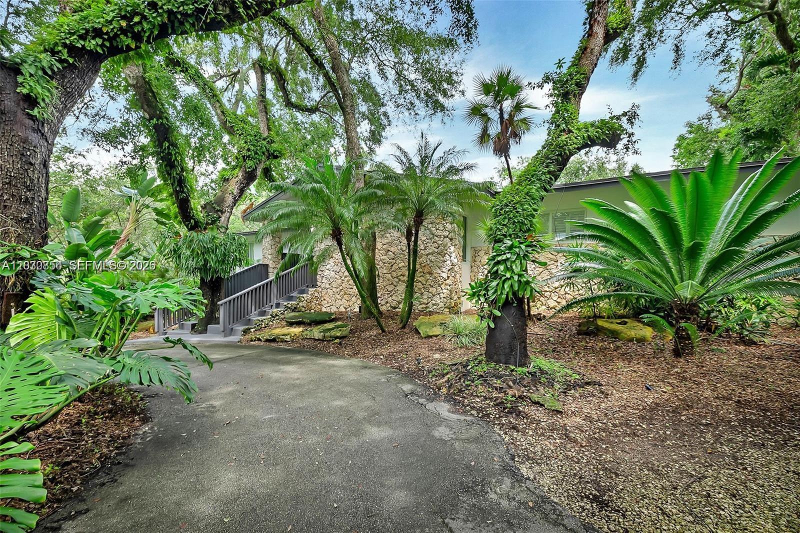 A stone-faced house exterior features a paved driveway, lush tropical landscaping, and wooden stairs — 6565 SW 134th Dr, Pinecrest FL 33156, PINECREST, FL