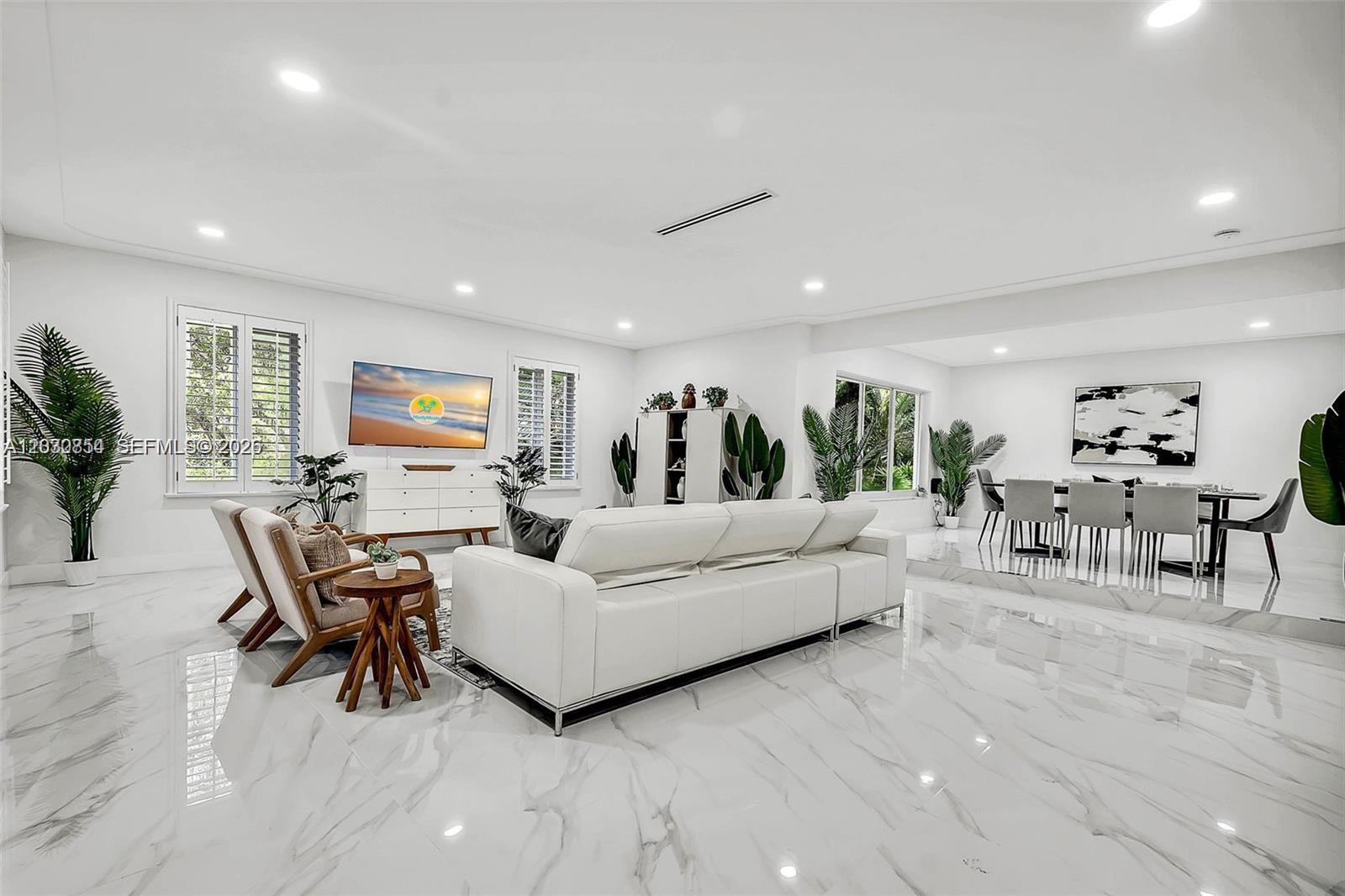 A modern, open-concept living and dining area features white marble flooring and minimalist decor — 6565 SW 134th Dr, Pinecrest FL 33156, PINECREST, FL
