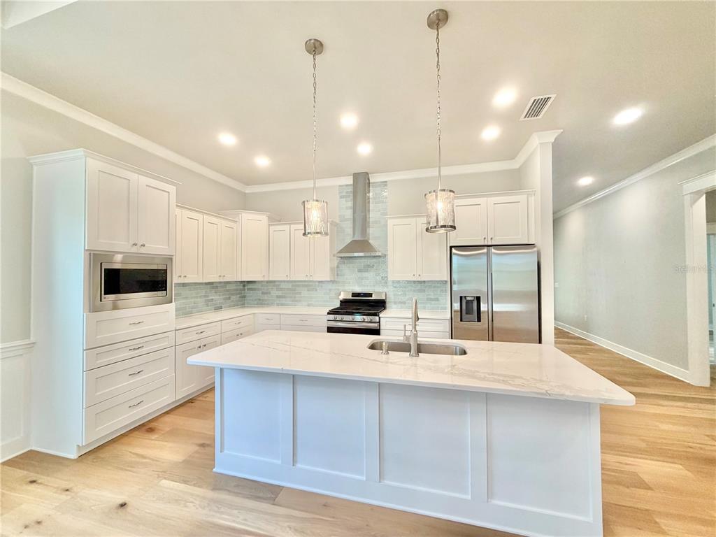 A modern kitchen features white cabinetry, a large marble-topped island, and stainless steel appliances — 2537 NW 48TH TERRACE, GAINESVILLE, FL
