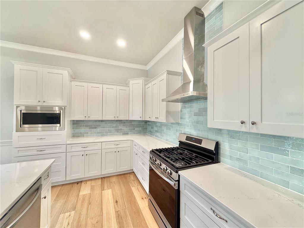 A kitchen features white cabinets, light blue subway tile backsplash, stainless steel appliances, and wood flooring — 2537 NW 48TH TERRACE, GAINESVILLE, FL