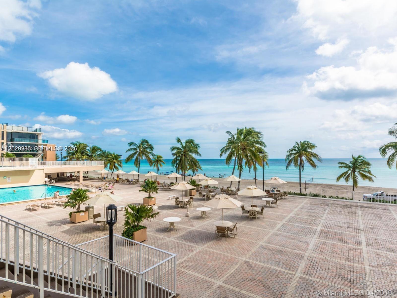 An outdoor patio with tables, umbrellas, and palm trees overlooks a swimming pool and beach — 2101 S Ocean Dr # 306, Hollywood FL 33019, HOLLYWOOD, FL