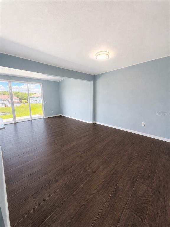 An empty room with light blue walls, dark wood-look flooring, and sliding glass patio doors — 872 CARIBBEAN DRIVE, DAVENPORT, FL