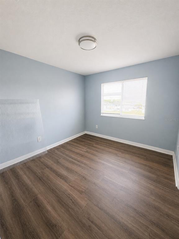 An empty bedroom features light blue walls, a window with blinds, and dark wood flooring — 872 CARIBBEAN DRIVE, DAVENPORT, FL