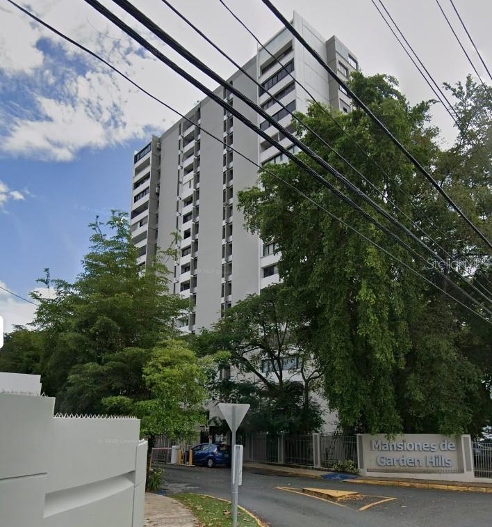 A tall, multi-story apartment building stands behind a gated entrance with mature trees — 1261 LUIS VIGOREAUX AVENUE UNIT 18D, GUAYNABO, PR