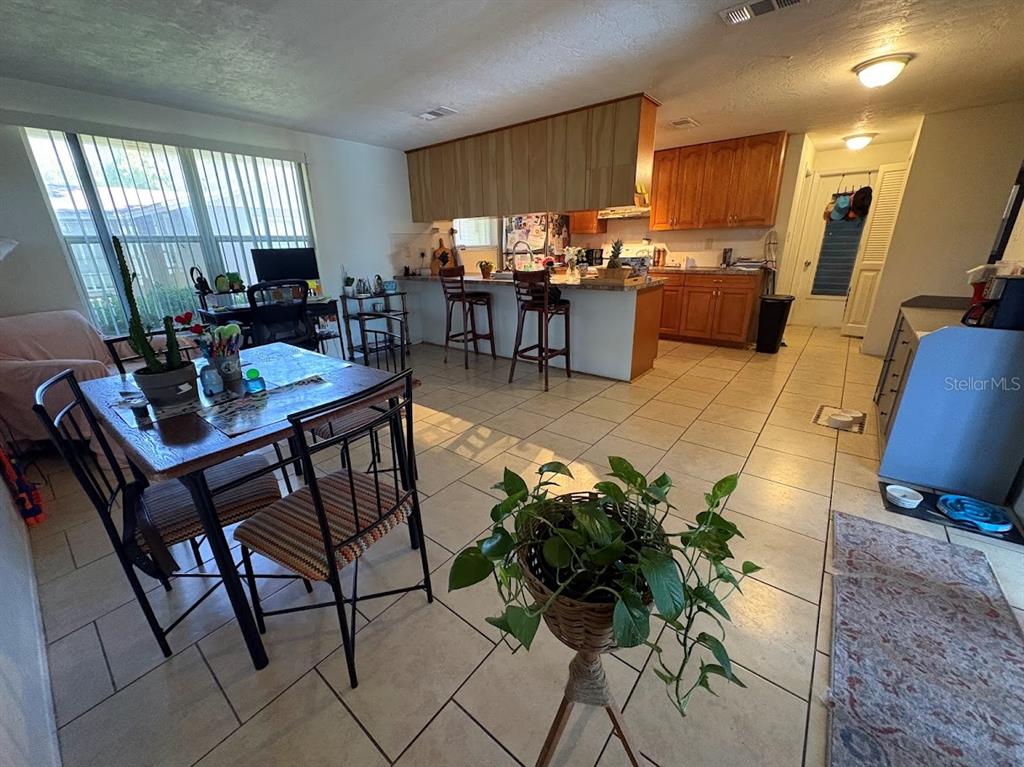 An open-concept kitchen and dining area features tile flooring, wood cabinetry, and a breakfast bar — 8220 FOX HOLLOW DRIVE, PORT RICHEY, FL