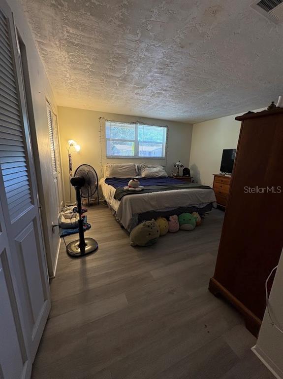 A bedroom features light wood-look flooring, a bed with plush toys, and a tall wooden wardrobe — 8220 FOX HOLLOW DRIVE, PORT RICHEY, FL