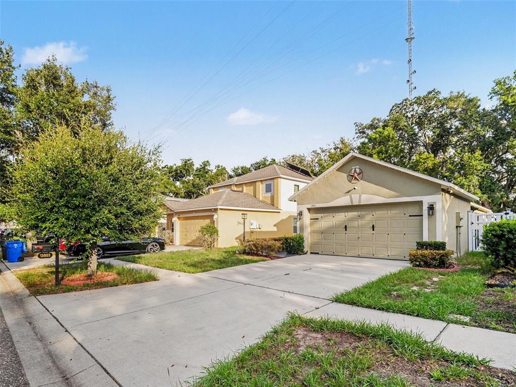 Two adjacent suburban houses with concrete driveways and attached garages under a clear blue sky — 13803 GENTLE WOODS AVENUE, RIVERVIEW, FL