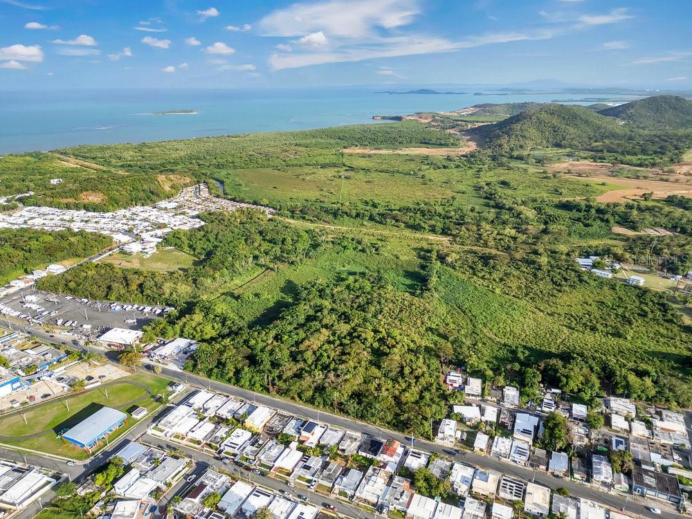 An aerial view shows a coastal landscape with residential neighborhoods, dense vegetation, and the ocean — PR-195 KM 1.9 BARRIO PUERTO REAL, FAJARDO, PR