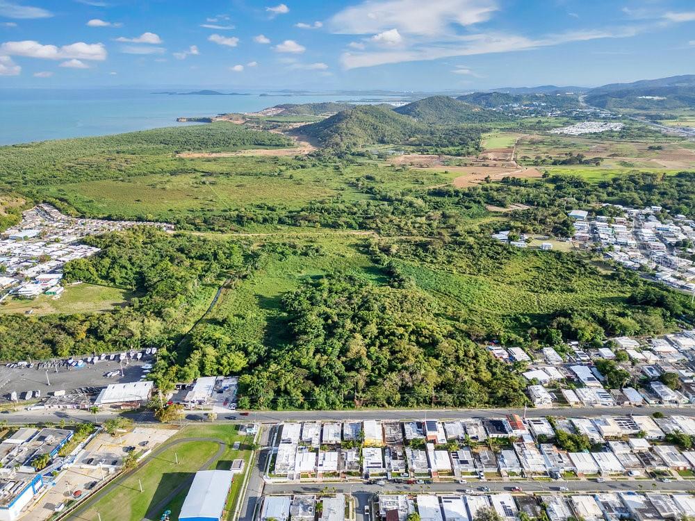 An aerial view shows a coastal landscape with residential neighborhoods, dense green vegetation, and mountains — PR-195 KM 1.9 BARRIO PUERTO REAL, FAJARDO, PR