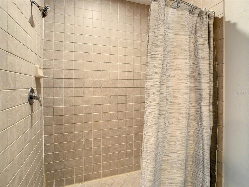 A shower stall features beige square wall tiles, a showerhead, and a patterned curtain — 7503 ATLANTIS WAY UNIT G103, KISSIMMEE, FL
